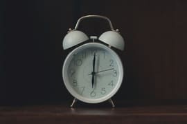 a white alarm clock sitting on top of a wooden table.