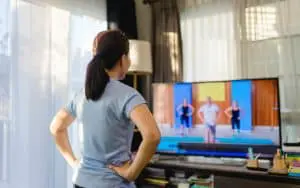 Video streaming Stay home.home fitness workout class live streaming online.Asian woman doing strength training cardio aerobic dance exercises watching videos on a smart tv in the living room at home.